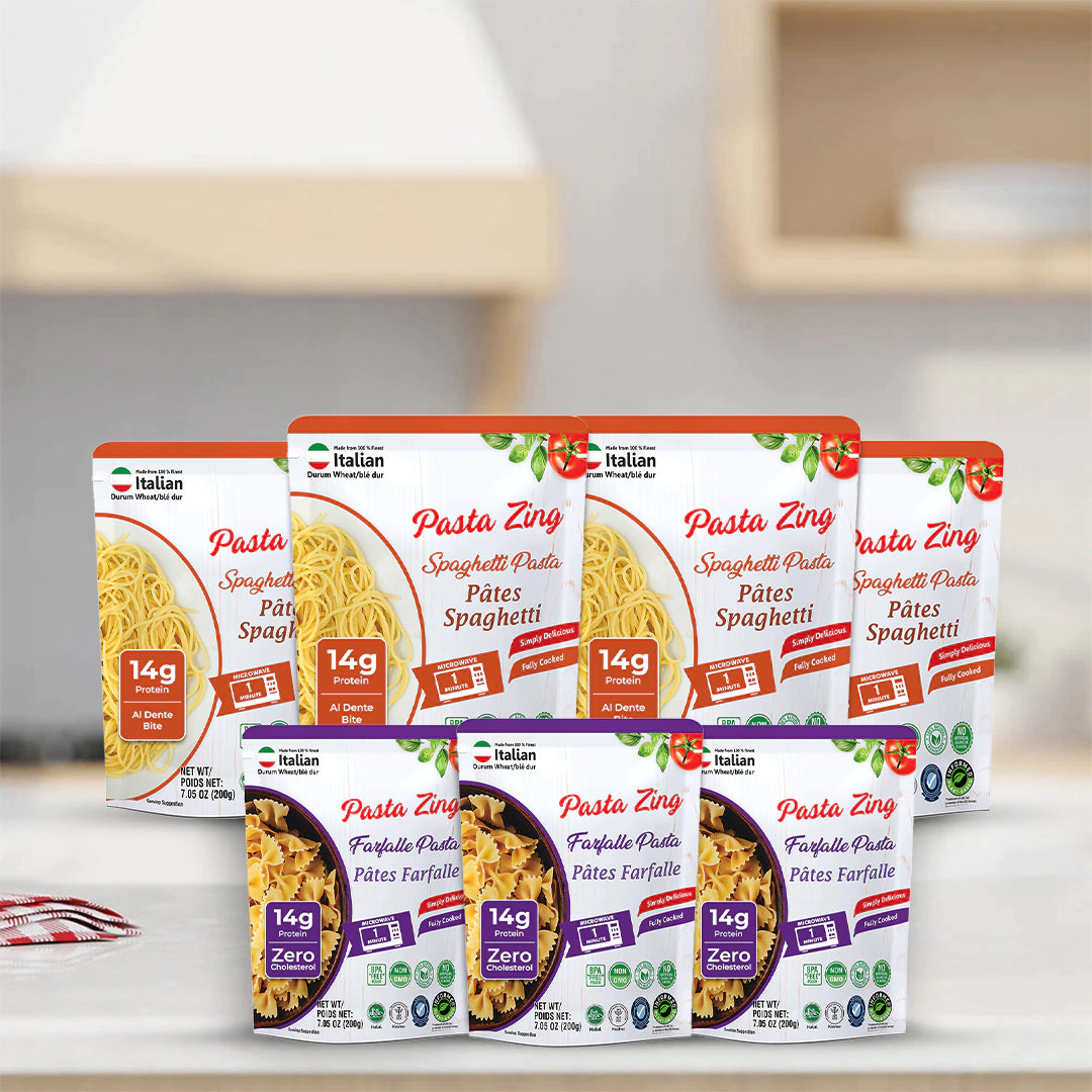 A bulk display of Pasta Zing pouches arranged on a white kitchen countertop with a blurred kitchen background. The back row contains four Spaghetti (orange) pouches, and the front row features three Farfalle (purple) pouches. Every pouch displays the "14g Protein" badge and the quick "1 Minute" microwave cook time, emphasizing the product’s convenience for meal prepping or large families.